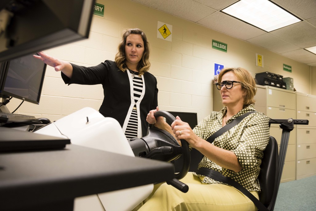 A female patient is instructed by a low vision specialist on a driving simulator