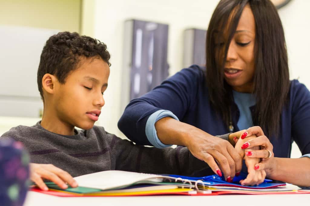 A teacher of the visually impaired works with a child who is blind to feel pages of a textured book