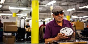 A man who is blind displays a clock he has assembled in the Chicago Lighthouse Industries factory.