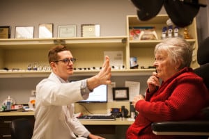 An older woman gets a low vision examination from an vision specialist. He holds his hand far out to the left to test her peripheral vision.