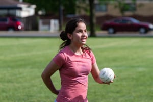 A teenage girl who is visually impaired smiles while holding a beep baseball.