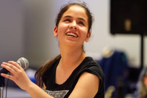 A teenage girl who is visually impaired smiles as she sings at the talent show in The Lighthouse's Summer in the City performance