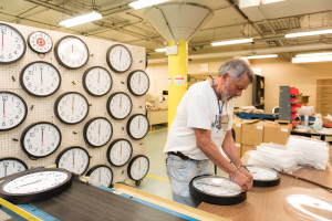 A clock factory employee adds the final piece to a clock on the assembly line
