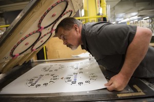 A man with low vision checks the alignment of clock faces before they are die cut