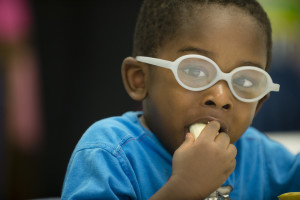 A preschool age child wearing glasses enjoys snack time at school