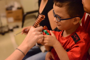 Young boy with glasses looks closely at a finger puppet during an eye exam