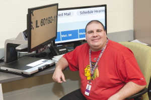 Worker at Chicago Lighthosue Illinois Tollway IPass facility smiling in front of his computer.