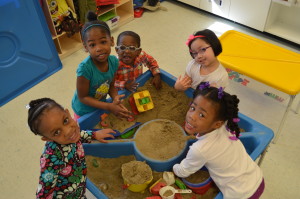 Five children in the preschool play around a sand table