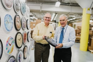 Two managers inspect a clock in front of a testing board that displays about a dozen fashion clocks prior to packaging