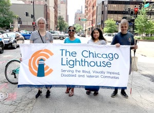 A group of four people from The Chicago Lighthouse holding a parade banner