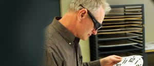 A visually impaired employee wearing cocoon glasses inspects a clock face dial