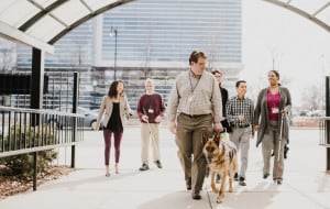 A small group of men and women walk under the archway of The Chicago Lighthouse. A german shepherd dog guide leads the way.