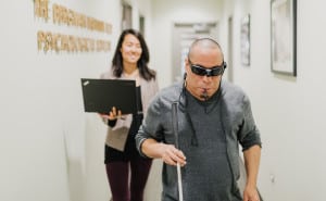 A man who is blind experiences his surroundings using Brainport technology while a researcher follows closely behind