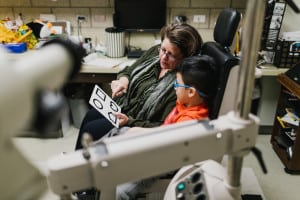A low vision optometrist shows large print flash cards to a young boy seated in an exam chair