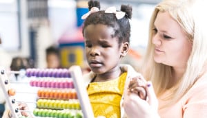A preschool girl who is blind plays with a colorful abacus with the assistance of her teacher