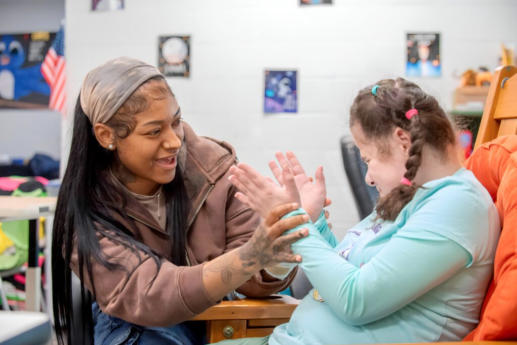 A girl who is blind claps her hands with her paraprofessional
