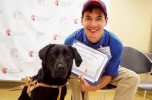 A college student holds up his scholarship certificate while posing with his guide dog