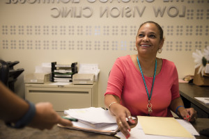 Carmen smiles from the front desk of the Low Vision Clinic