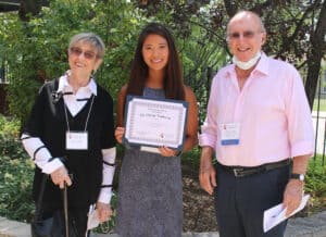 A college student stands between her scholarship donors with her certificate in hand and a big smile on her face.