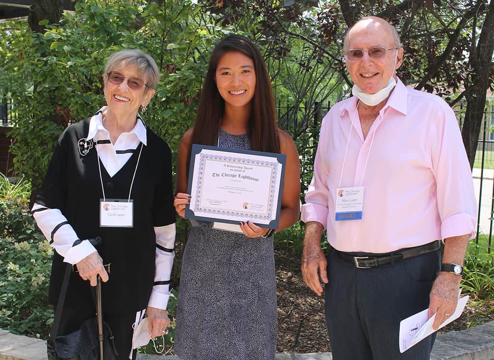 A college student stands between her scholarship donors with her certificate in hand and a big smile on her face.