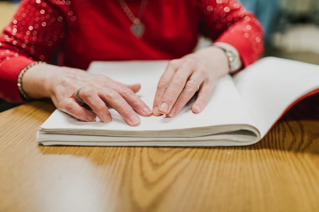 A close up photo of hands on top of page in a Braille book. 