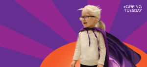 A preschool girl who is visually impaired and has albinism wears a superhero cape against a comic style background