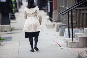 back view of a person who is blind walking with her white cane sweeping side to side