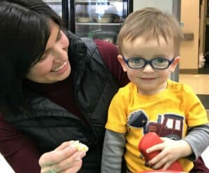 Young child who is visually impaired, wearing glasses, smiling as he sits on his mom's lap
