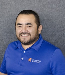 Ricardo smiling in front of a dark background wearing a blue polo
