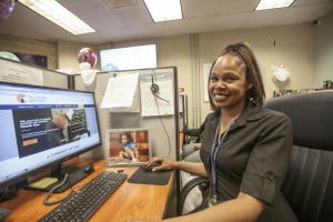 A Veteran employed in one of our Customer Care Centers smiles next to her computer.