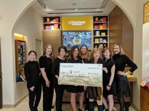 Eight women from L'Occitane present an oversized check to Jennifer Miller from The Chicago Lighthouse in a beautiful L'Occitane store