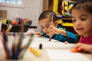 Two children paint together in a classroom.