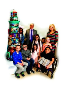 President/CEO Dr. Janet Szlyk and Chairman of the Board Gary Rich pose in front of a painted Lighthouse sculpture with several young children, many who are disabled