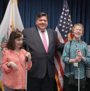 Two summer interns in our CRIS radio program pose with Governor JB Pritzker in front of the US and Illinois state flags