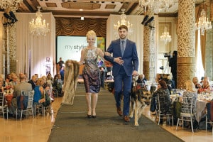 Ben walks down a fashion runway with his guide dog and a model at The Lighthouses' FLAIR fashion show