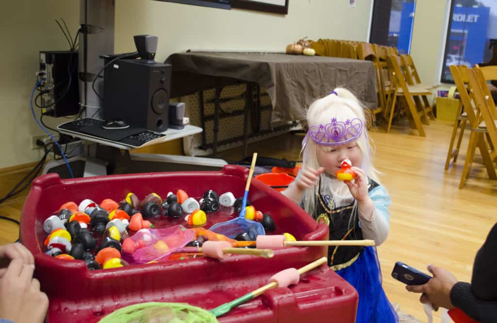 A young girl dressed as a princess smiles while holding a rubber duck she caught while playing a duck-catching game.