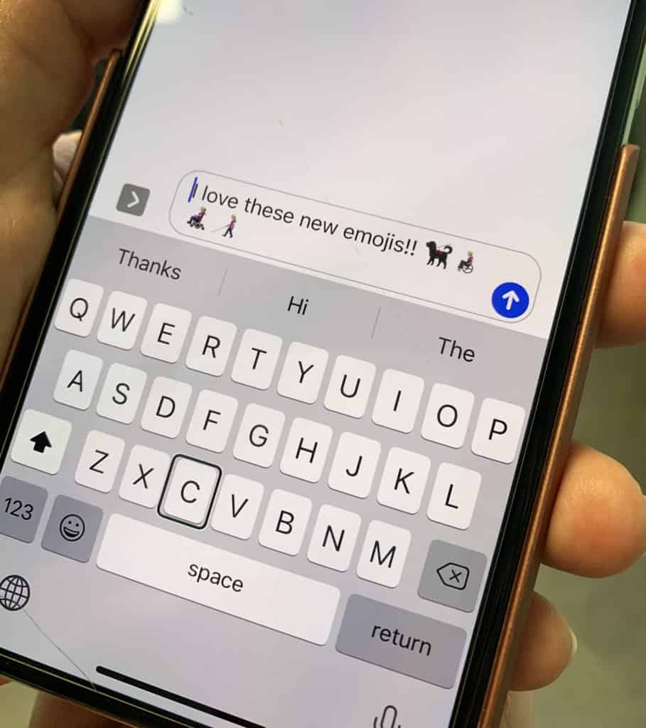 A screen of an iPhone is shown. A text message is shown with the text "I love these new emojis!!" and is followed by the following emojis: a guide dog, a woman sitting in a wheelchair, a man sitting in a motorized wheelchair, and a woman using a white cane. 