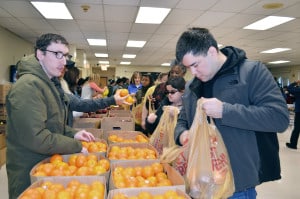 Two Chicago Lighthouse employees pickup oranges in boxes and put them in bags as they go through the food drive line.
