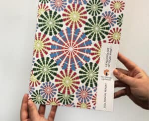 An annual report with images of kaleidoscopes is held in two hands