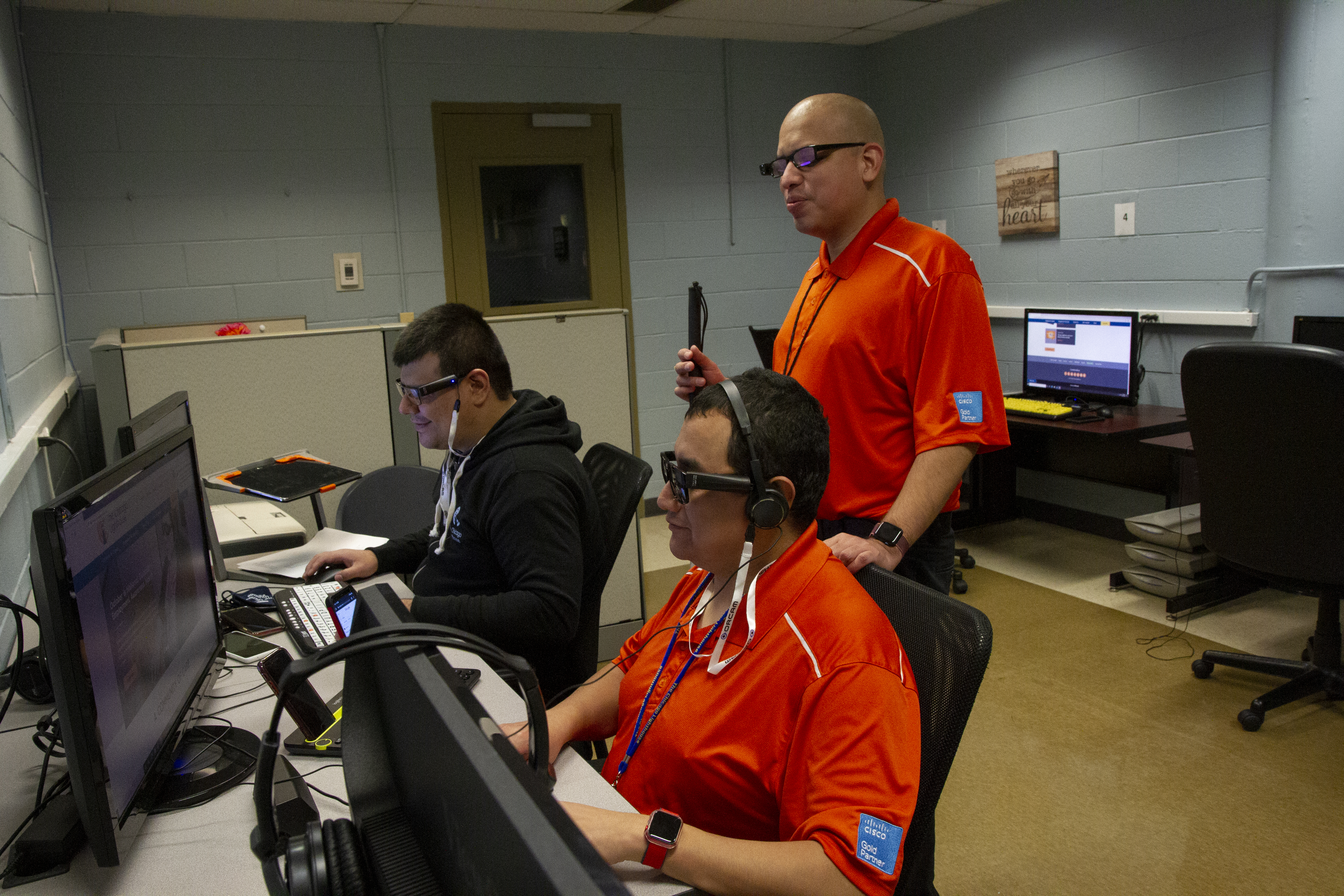 Two employees who are visually impaired working at computers, while another employee stands behind.