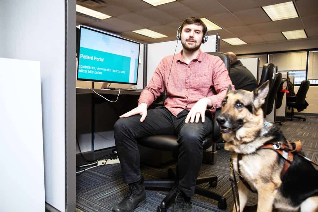 A call center agent is seated at his desk with his guide dog.