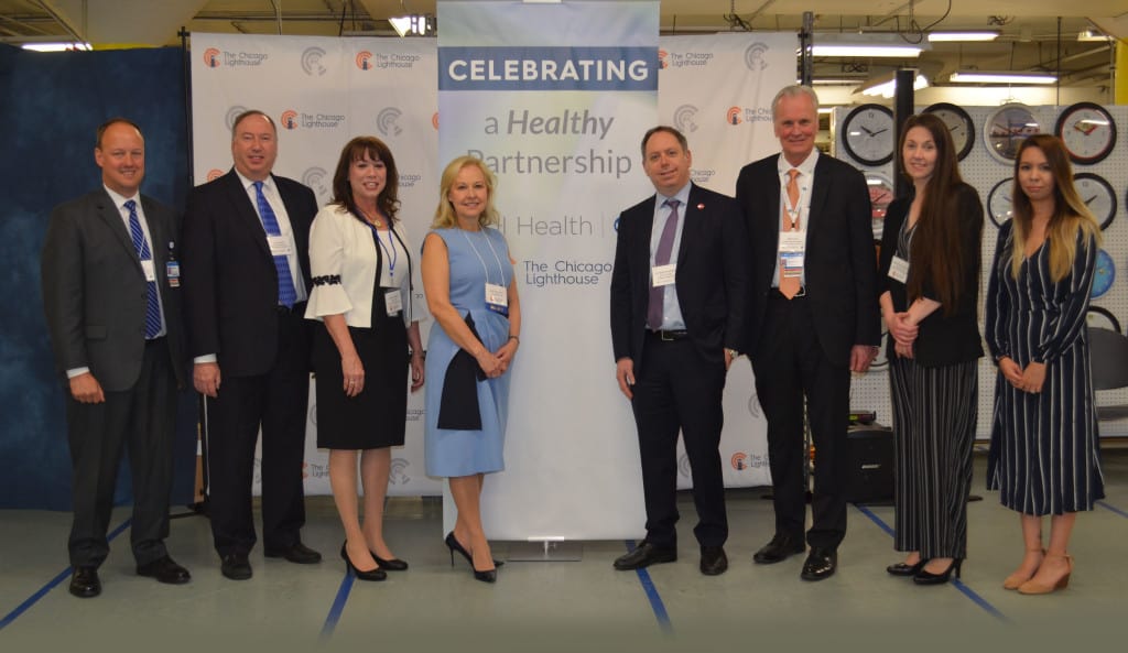 Eight executives pose in front of a tall banner that reads "Celebrating a Healthy Partnership" during a ribbon cutting ceremony for the new UI Health Call Center