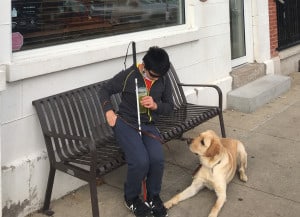Isaac sitting on a bench, Flyer, his guide dog, sitting in front