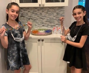 Twin sisters hold their beaded mask holders and smile