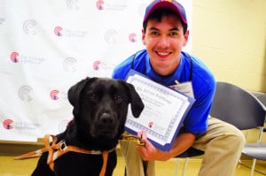 a past scholarship recipient sitting and smiling holding his award, next to his guide dog
