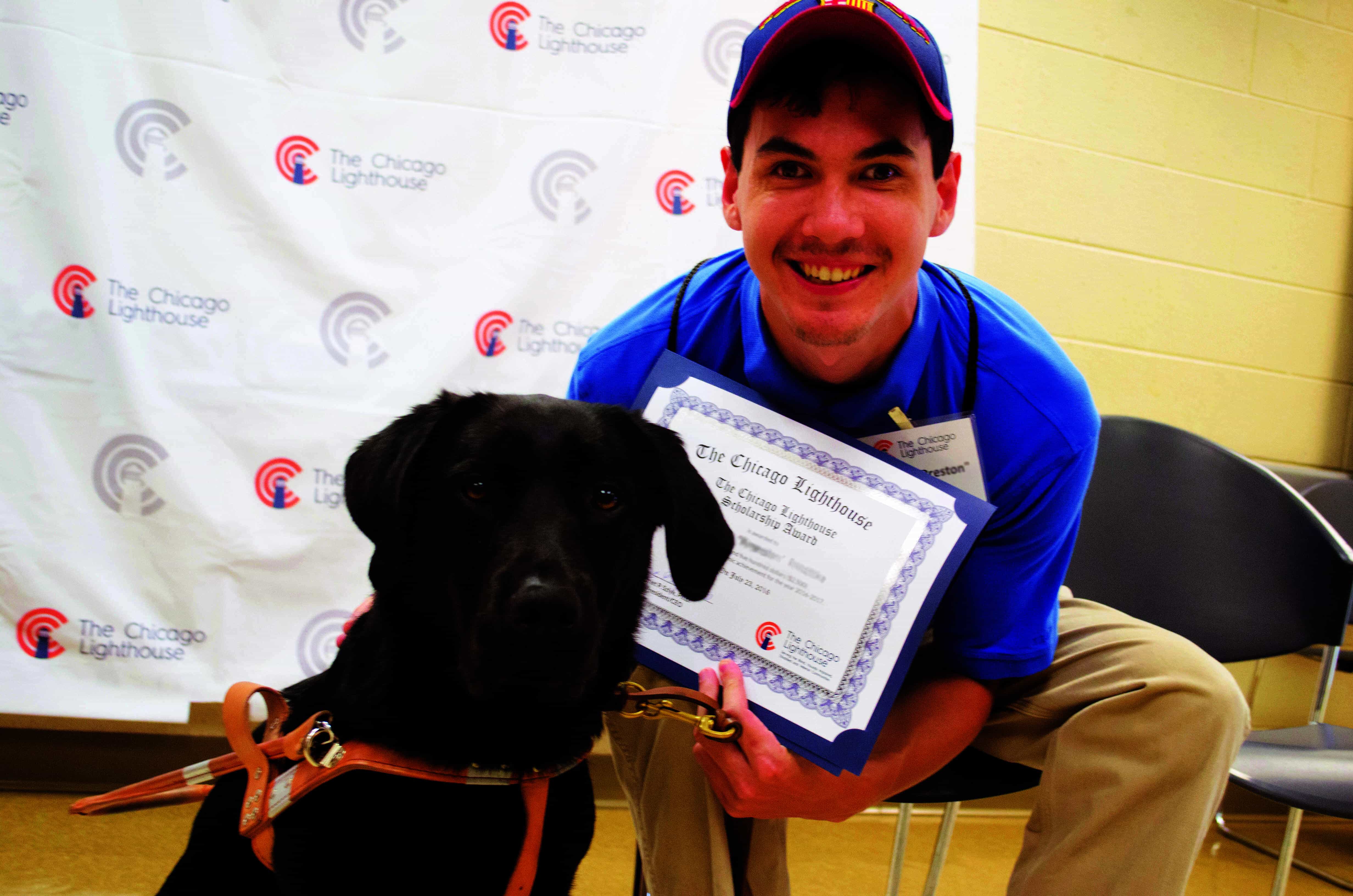 a past scholarship recipient sitting and smiling holding his award, next to his guide dog