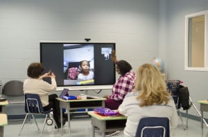 The Lighthouses' preschool teachers conducting e-learning over zoom, and sit in front of a large screen, talking with their students