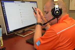 Geovanni wearing a headset and sitting in front of a computer, also using his phone