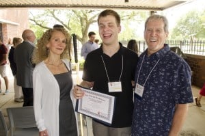 Jack smiling at the summer scholarship ceremony, holding his scholarship certificate and standing between Michelle and Gary Rich