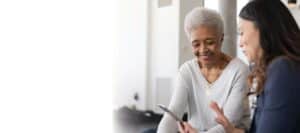 An older African American woman has a conversation with her female health care provider. Both women are smiling.